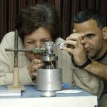 La Doctora en Ciencias Físicas Mayra Hernández y el maestro Carlos Canino con el microscopio de efecto túnel. Linterna en mano, observe que la punta de la aguja está lo suficientemente próxima a la muestra como para iniciar el barrido.